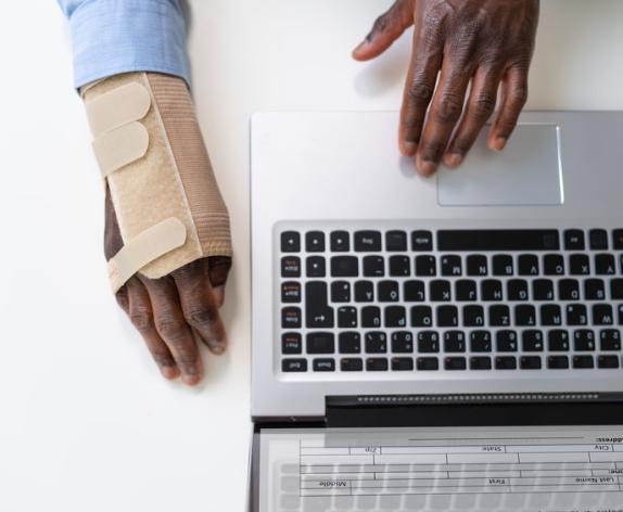 An office worker's hands on a laptop. One hand has a brace.